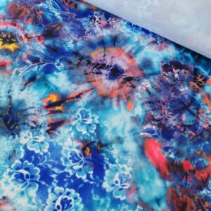 Tissu lycra très coloré dans des ton principalement de bleu et turquoise avec des taches colorées (comme de l'encre) orangées. Quelques motifs de fleurs en impression. Envers blanc.