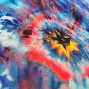 Tissu lycra très coloré dans des ton principalement de bleu et turquoise avec des taches colorées (comme de l'encre) orangées. Zoom sur l'une de ces taches.