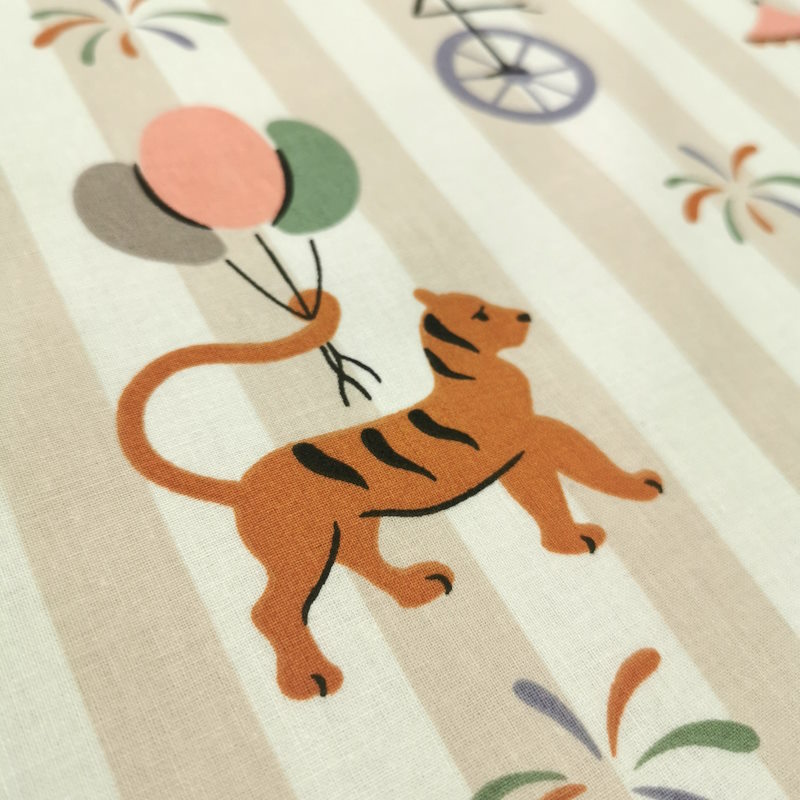 Animaux du cirque Tissu à rayure, avec par dessus des motifs d'animaux du cirque portant des ballons, des sucreries ou sur des monocycles.