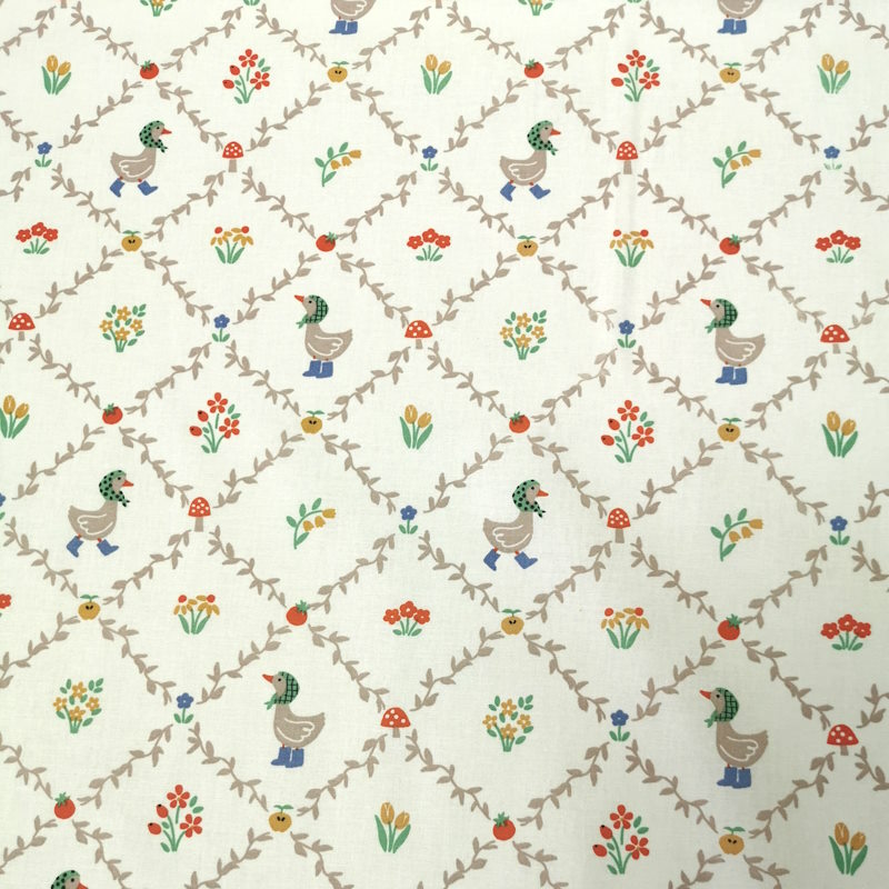 Petites Oies Tissu avec des motifs en quadrillage formant des losanges, avec au centre des petites oies mignonnes et des fleurs colorées.